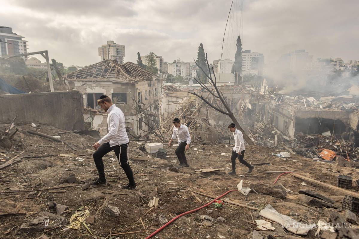 $!Personas caminando entre las ruinas de edificios dañados por un ataque con misiles iraníes en Rehovot, Israel.