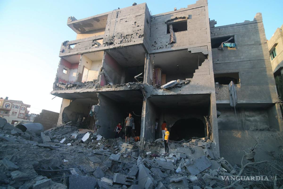 $!Palestinos de pie junto a un edificio destruido en un ataque aéreo israelí en la frontera de Rafah, en la Franja de Gaza, el lunes 16 de octubre de 2023.