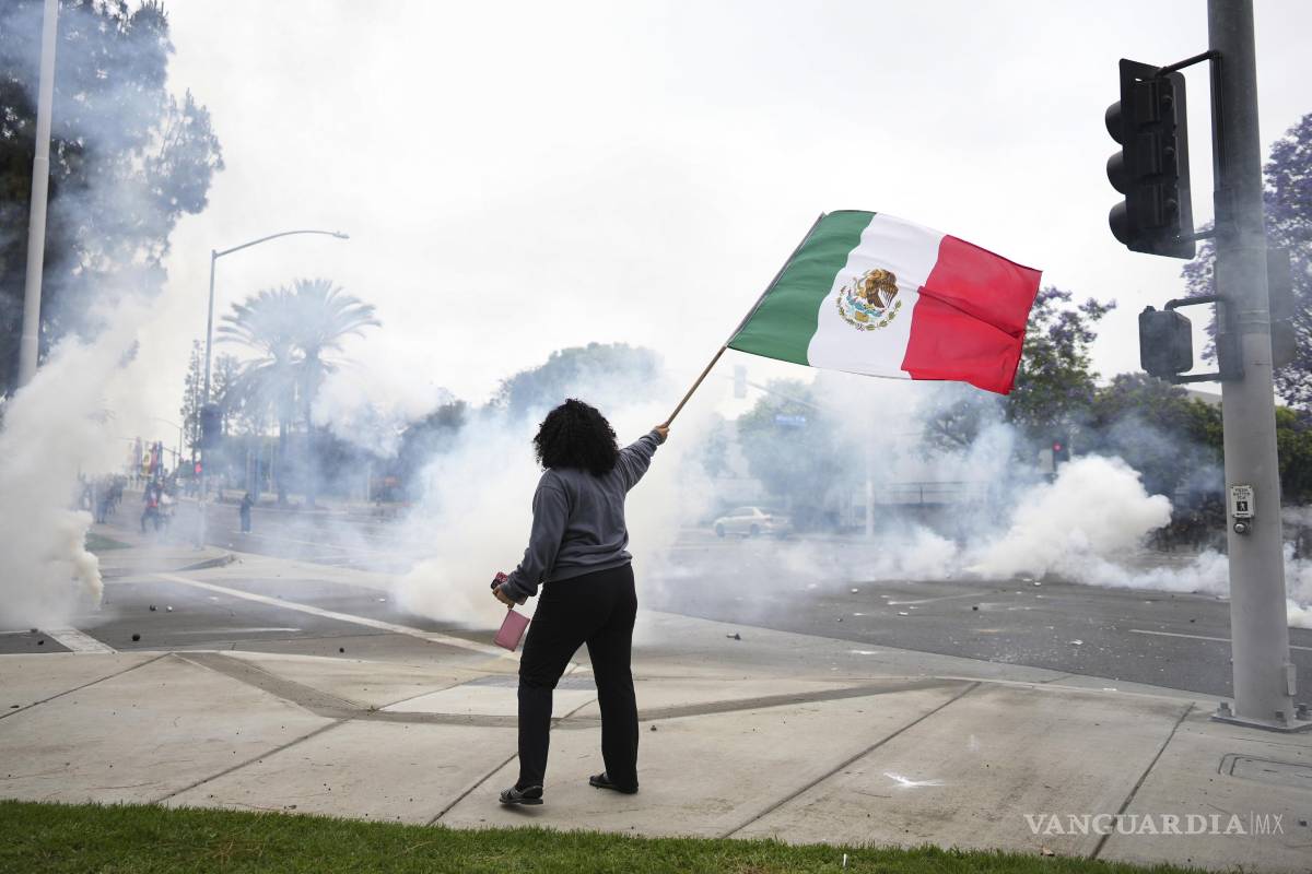$!Una mujer ondea una bandera mexicana en medio de gases lacrimógenos lanzados por las fuerzas del orden durante una protesta en Paramount, California.