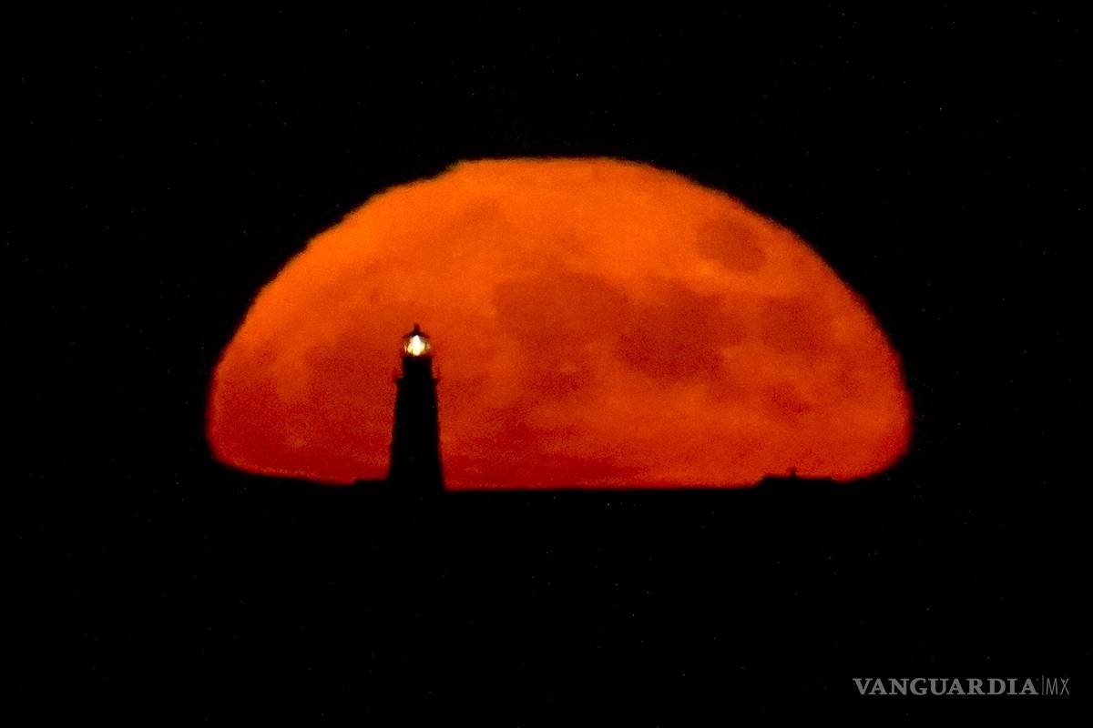 $!Una luna llena se eleva detrás de la luz de Boston en la noche en Winthrop, Massachusetts. Durante el fenómeno conocido como la “Luna de Fresa”.