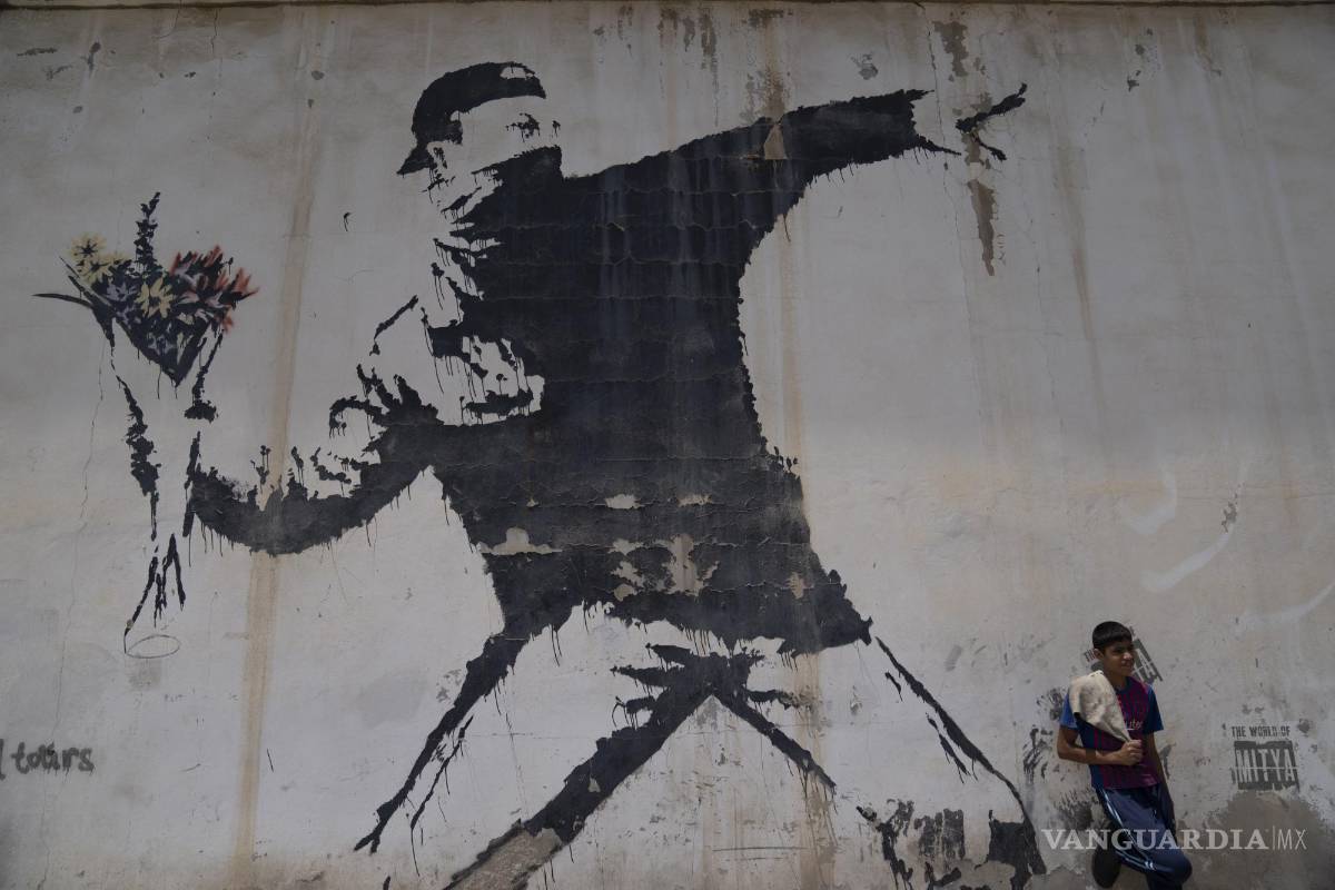 $!Un joven palestino descansa bajo un mural del reservado artista de grafiti británico Banksy en una gasolinera en la ciudad cisjordana de Belén.