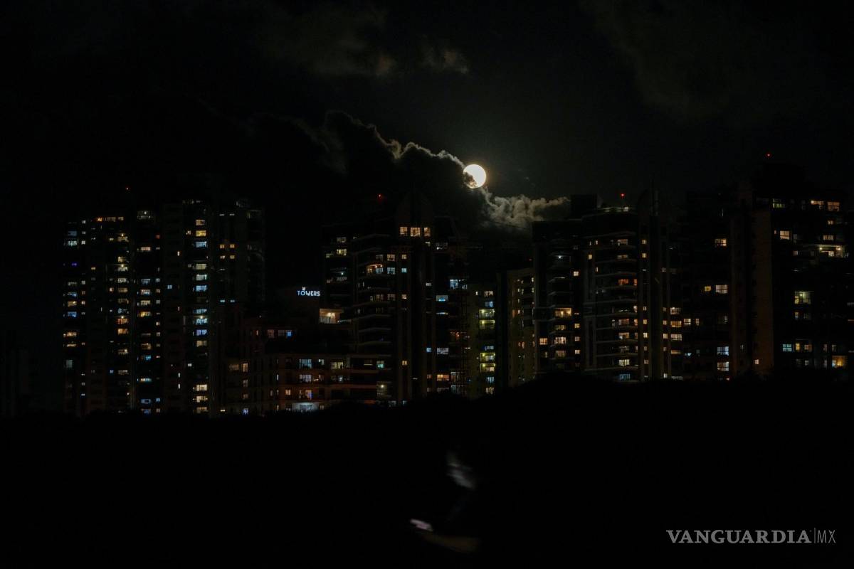 $!Una mujer camina con su teléfono inteligente mientras una superluna está parcialmente oscurecida por las nubes en el cielo en Hadera, Israel.