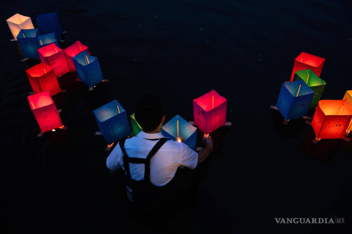 $!Un voluntario coloca linternas de papel que flotan a lo largo del río Motoyasu frente a la Cúpula de la Bomba Atómica en el 80.º aniversario del bombardeo atómico.