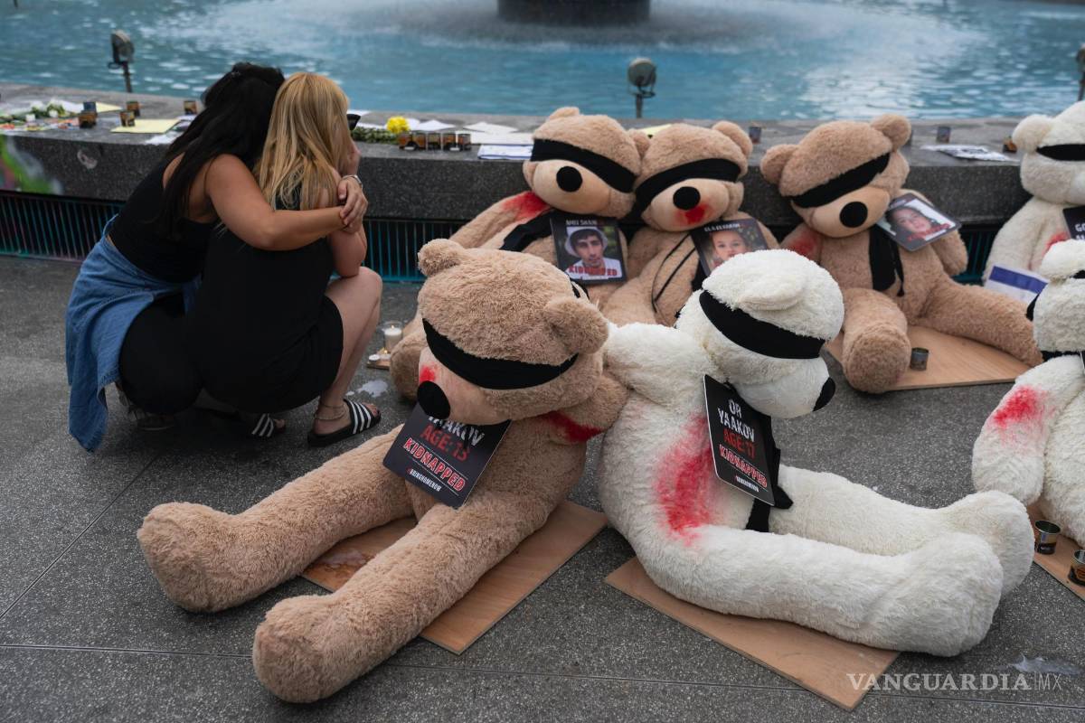 $!Dos mujeres se abrazan junto a una instalación de ositos de peluche gigantes con los ojos vendados con fotografías de israelíes cautivos en Gaza, en Tel Aviv, Israel.