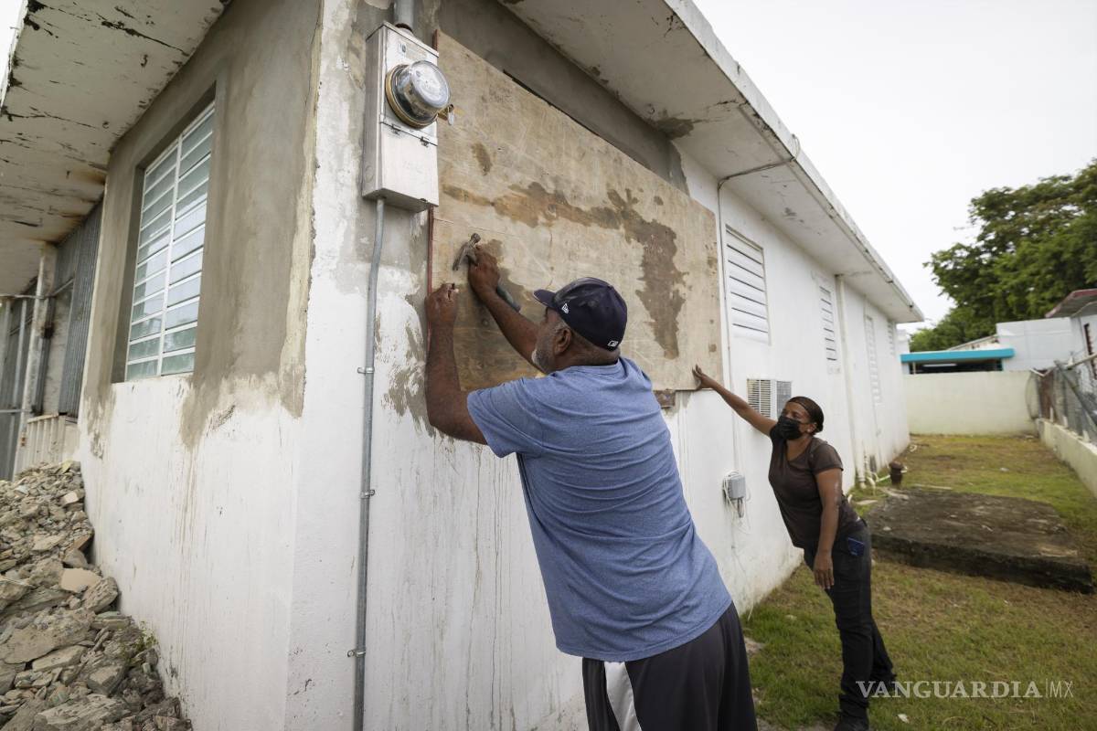 $!Residentes cubren una ventana de su casa ante la inminente llegada de la tormenta tropical Fiona.