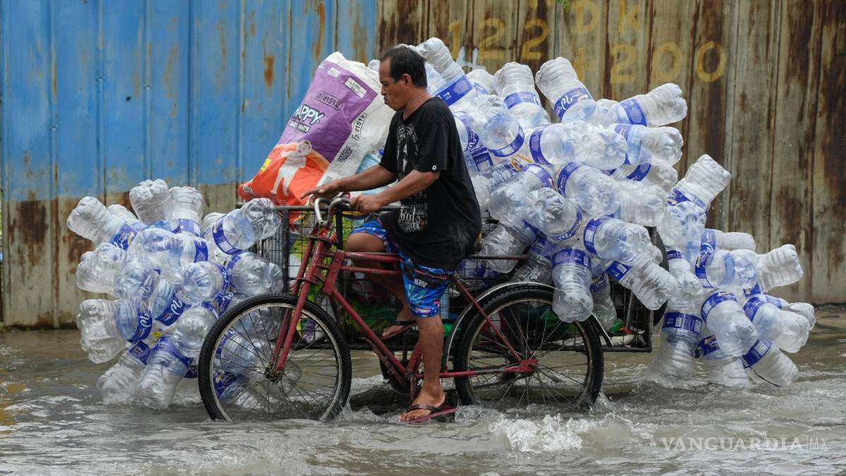 $!Un hombre utiliza su bicitaxi para transportar contenedores de plástico usados a lo largo de una calle inundada en la ciudad de Valenzuela, Filipinas.