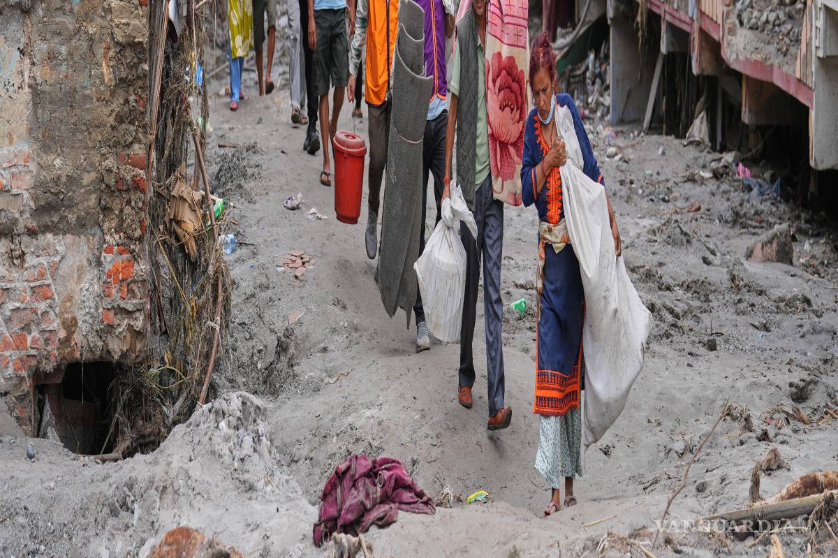 $!Residentes cargan con las pertenencias que pudieron rescatar de sus casas, llenas de lodo y escombros, tras las inundaciones repentinas, en Devighat, Nepal.