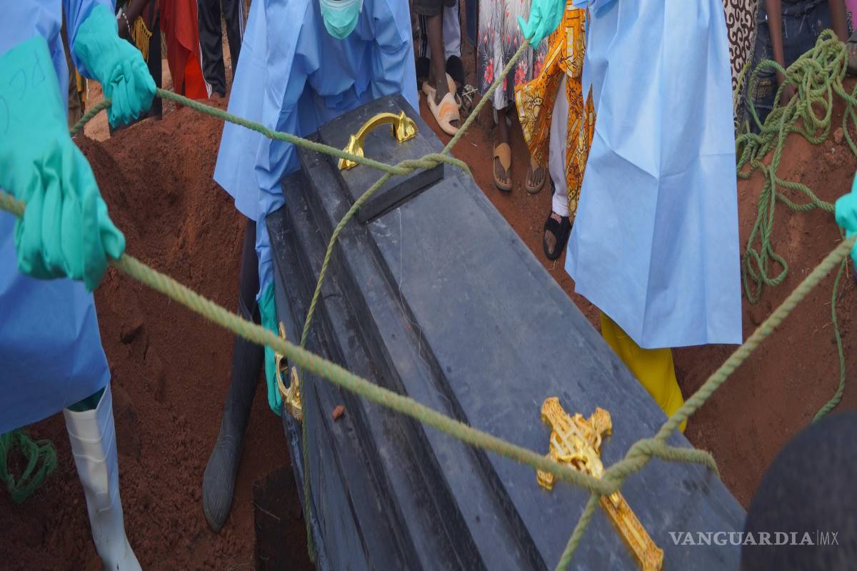 $!Varias personas vestidas con equipos de protección bajan a una tumba el féretro de Jeannine Katusabe, quien murió de ébola, durante su entierro en Bunia.