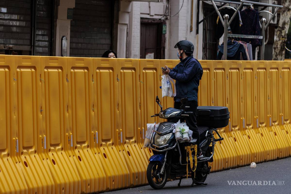 $!Un hombre entrega comida a las personas en el recinto en cuarentena en medio del cierre, en el lado de Puxi de la ciudad, en Shanghái, China.