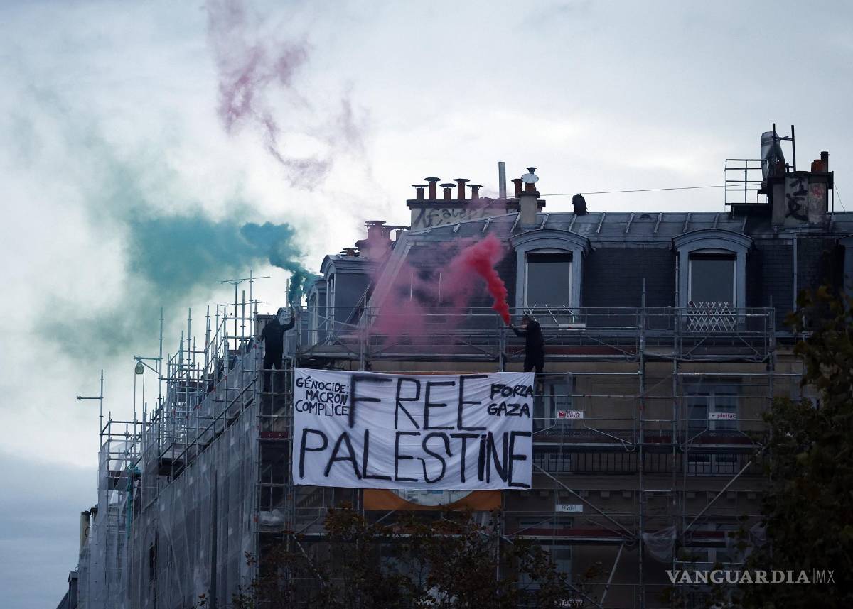 $!Dos manifestantes queman velas de humo en lo alto de un edificio junto a una pancarta de “Palestina libre”, para apoyar al pueblo palestino, en París, Francia.