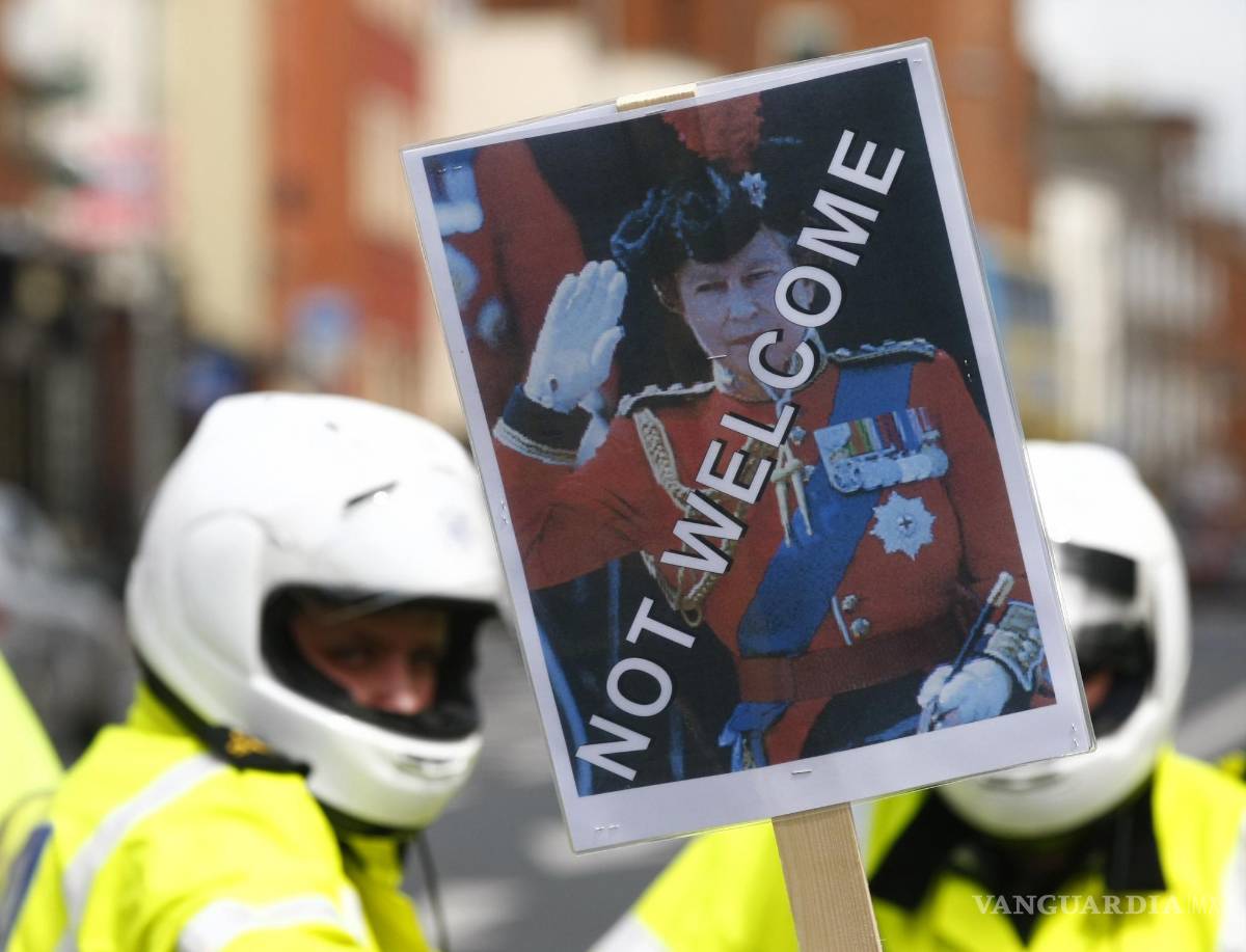 $!Un manifestante sostiene una pancarta con la imagen de la reina Isabel II frente a la policía en Dublín el 17 de mayo de 2011. AP/Tim Hales