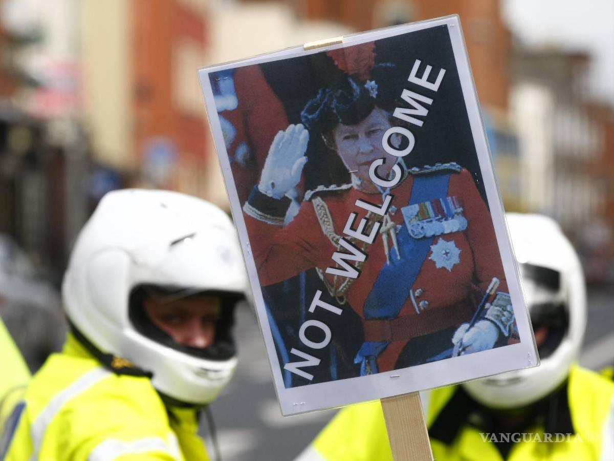 $!Un manifestante sostiene una pancarta con la imagen de la reina Isabel II frente a la policía en Dublín el 17 de mayo de 2011. AP/Tim Hales