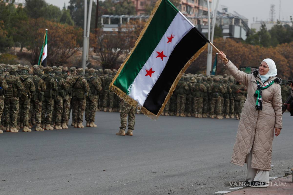 $!Una mujer y miembros del nuevo ejército sirio se forman antes del desfile militar por las celebraciones del año del derrocamiento del expresidente Bashar al-Assad
