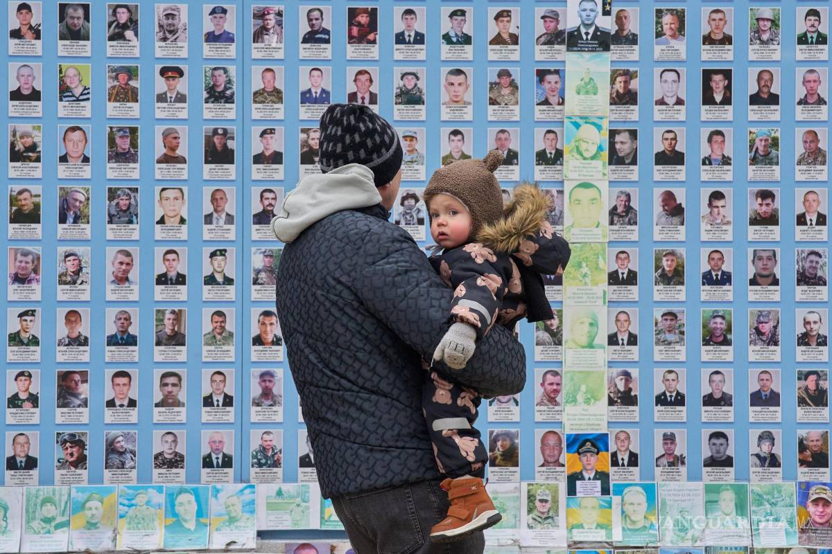 $!Un hombre sostiene a su hijo en el Muro Conmemorativo de los Defensores Caídos de Ucrania y muestra fotos de sus compañeros caídos en Kiev, Ucrania.