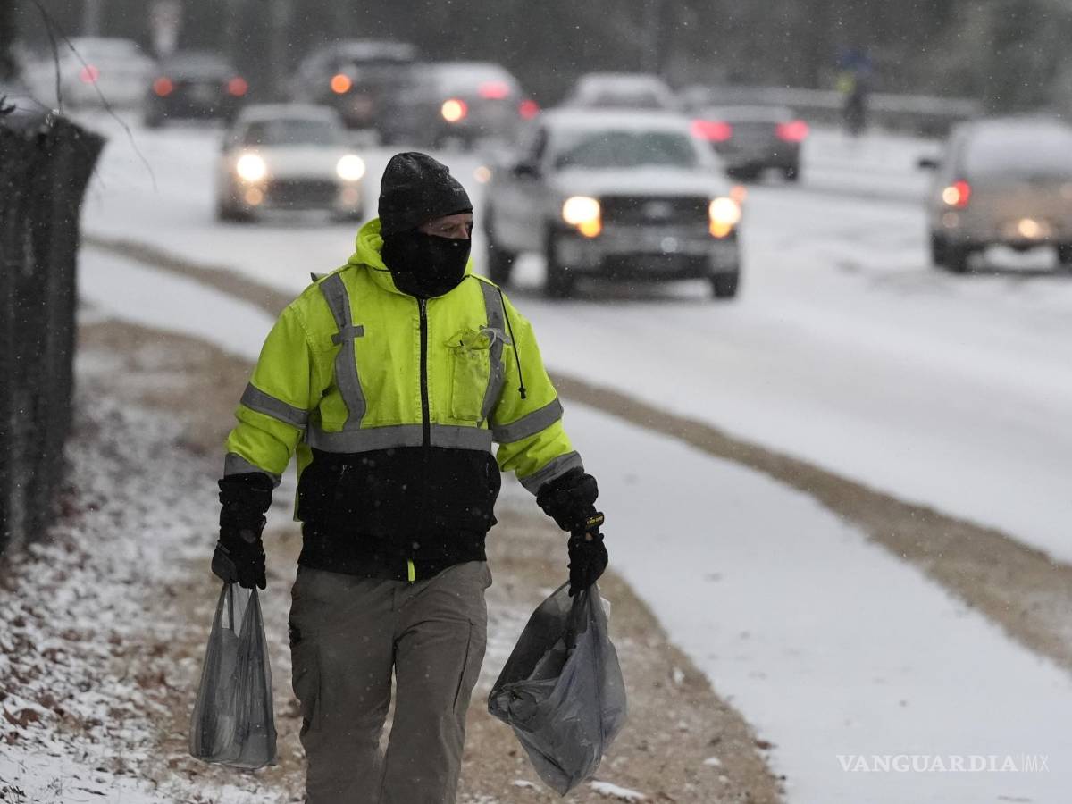 $!na persona camina por la acera con compras mientras cae nieve durante una tormenta invernal el martes 21 de enero de 2025, en Tucker, Georgia.