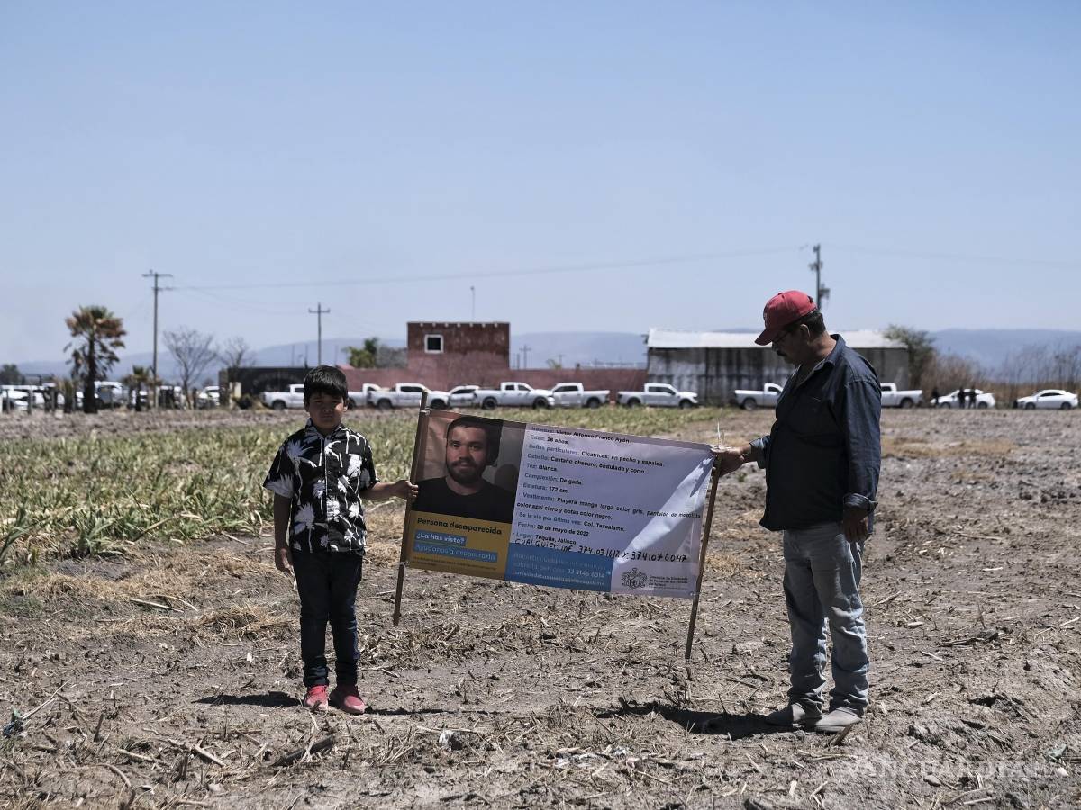$!Dos personas sostienen una fotografía de un familiar desaparecido afuera del Rancho Izaguirre, donde se descubrieron restos óseos en Teuchitlán, Jalisco.