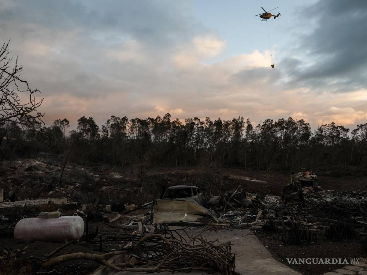 $!Un helicóptero arroja agua sobre puntos calientes cerca de casas quemadas en Kula, Hawái.
