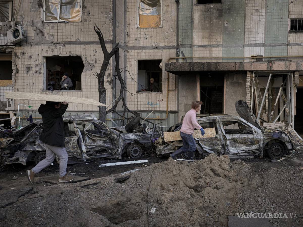 $!Gente carga tablones para cubrir las ventanas de un edificio dañado por una bomba el día anterior en Kiev, Ucrania.