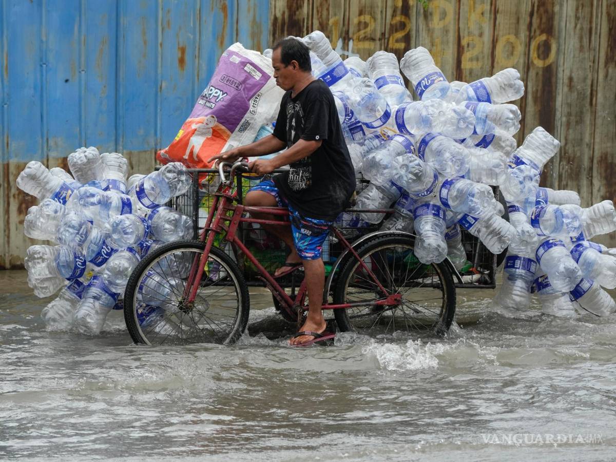 $!Un hombre utiliza su bicitaxi para transportar contenedores de plástico usados a lo largo de una calle inundada en la ciudad de Valenzuela, Filipinas.
