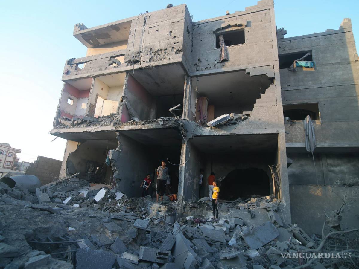 $!Palestinos de pie junto a un edificio destruido en un ataque aéreo israelí en la frontera de Rafah, en la Franja de Gaza, el lunes 16 de octubre de 2023.