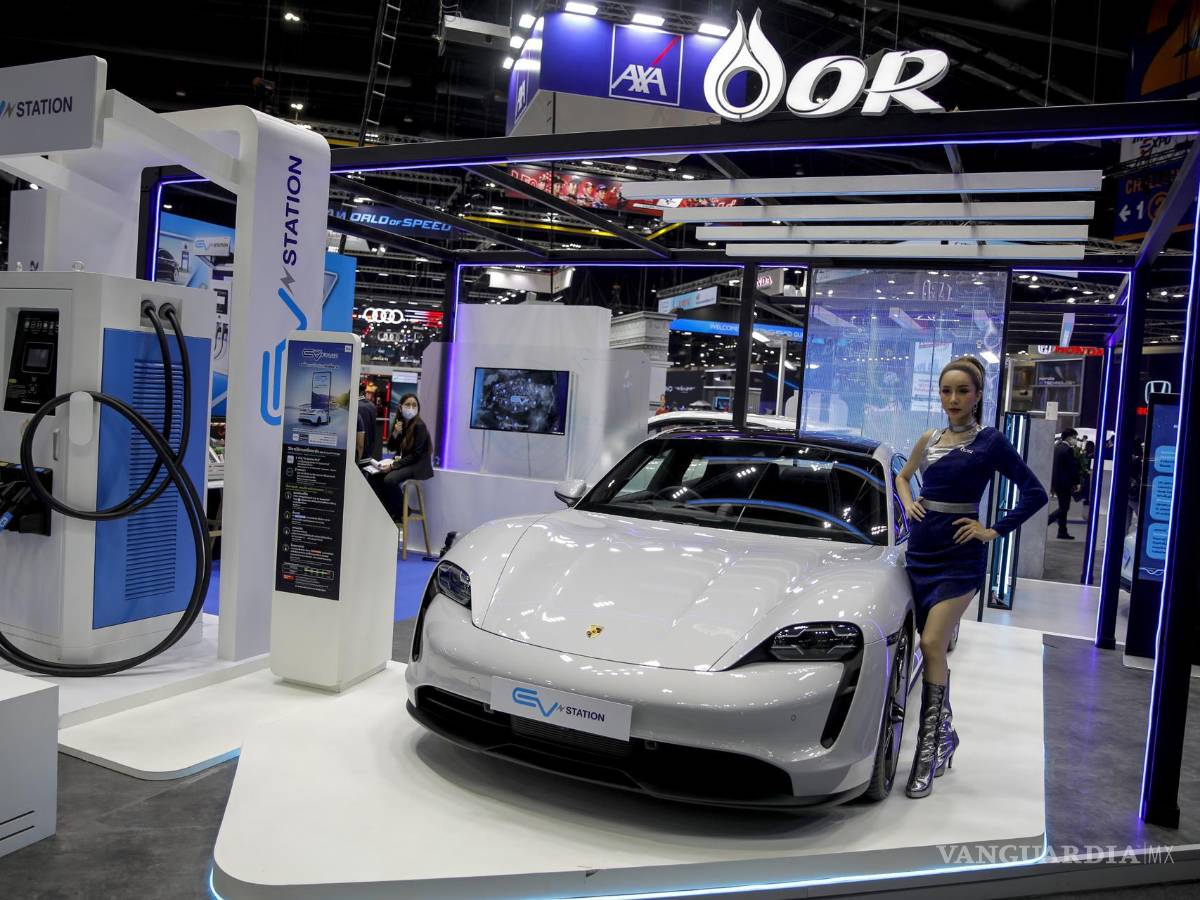 $!Un modelo se encuentra junto a un Porsche Cayman eléctrico en una estación de carga, en la 39.ª Exposición Internacional del Automóvil de Tailandia.