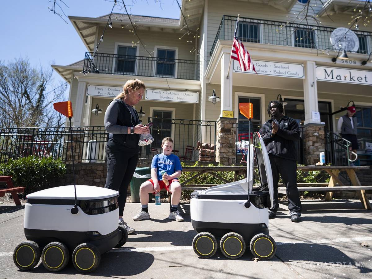 $!30 de marzo de 2020. Personas reciben comida de robots de reparto de alimentos, famosos durante la pandemia, en el mercado Broad Branch Market en Washington.