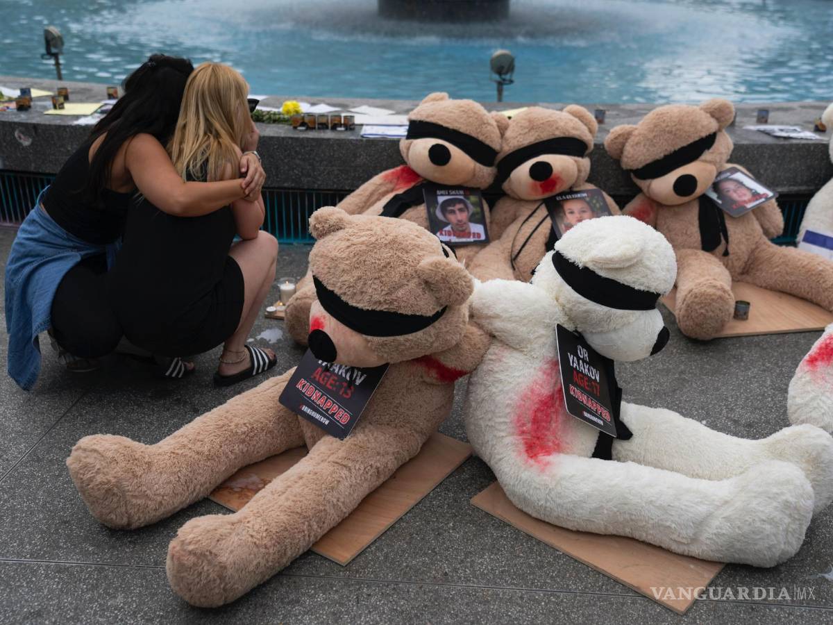 $!Dos mujeres se abrazan junto a una instalación de ositos de peluche gigantes con los ojos vendados con fotografías de israelíes cautivos en Gaza, en Tel Aviv, Israel.