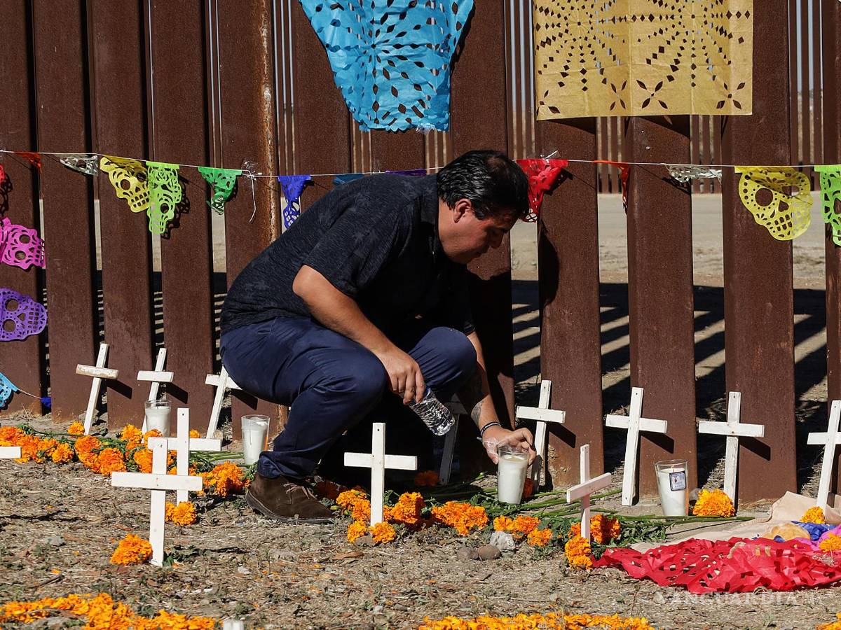 $!Un activista coloca una veladora en una ofrenda de Día de Muertos hoy, junto al muro fronterizo en Playas de Tijuana (México).