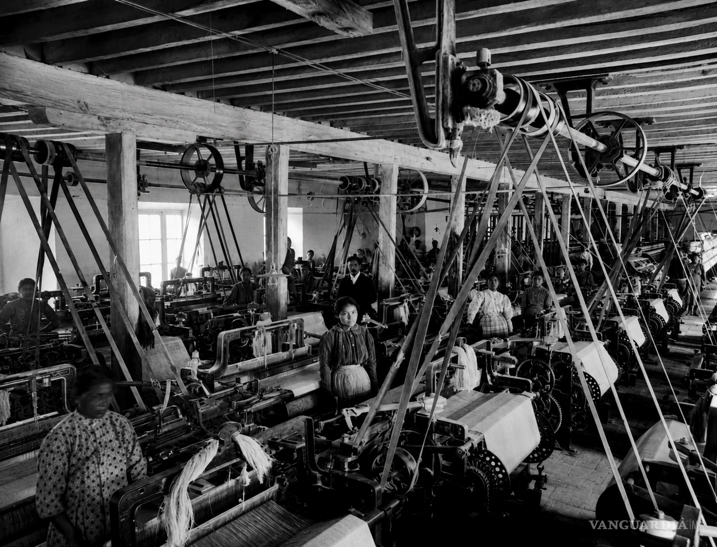 $!Trabajadoras entre los telares de la fábrica La Hibernia, en Saltillo, hacia 1905. El sistema de bandas y poleas que domina el espacio revela la nueva disciplina industrial: la fábrica concentró máquinas, horarios y trabajadores bajo una misma autoridad, mientras numerosas mujeres sostuvieron una producción que la memoria local ha contado con mayor frecuencia a través de sus propietarios que de quienes operaban los telares.