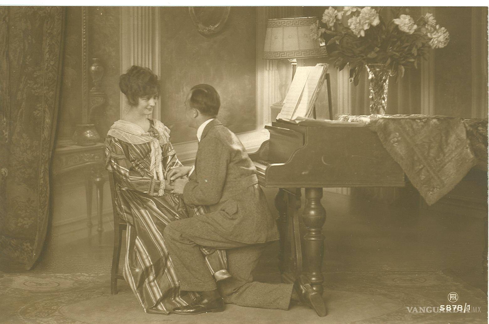 $!La mujer que aparece en esta postal parece ser la misma que la de la imagen anterior. Incluso hay un piano, aunque el diseño es diferente. Destaca un hombre que aparece hincado sobre la pierna derecha. En el reverso, con fecha 25 de octubre de 1920, parte del mensaje dice: “Nenita, ¿Por qué crees que no te extrañé? Si tú eres la única que me consuela y que me anima (...). Dime cuando vienes, pues ya sabes que yo soy muy pesimista, y temo a algunos acontecimientos futuros”.