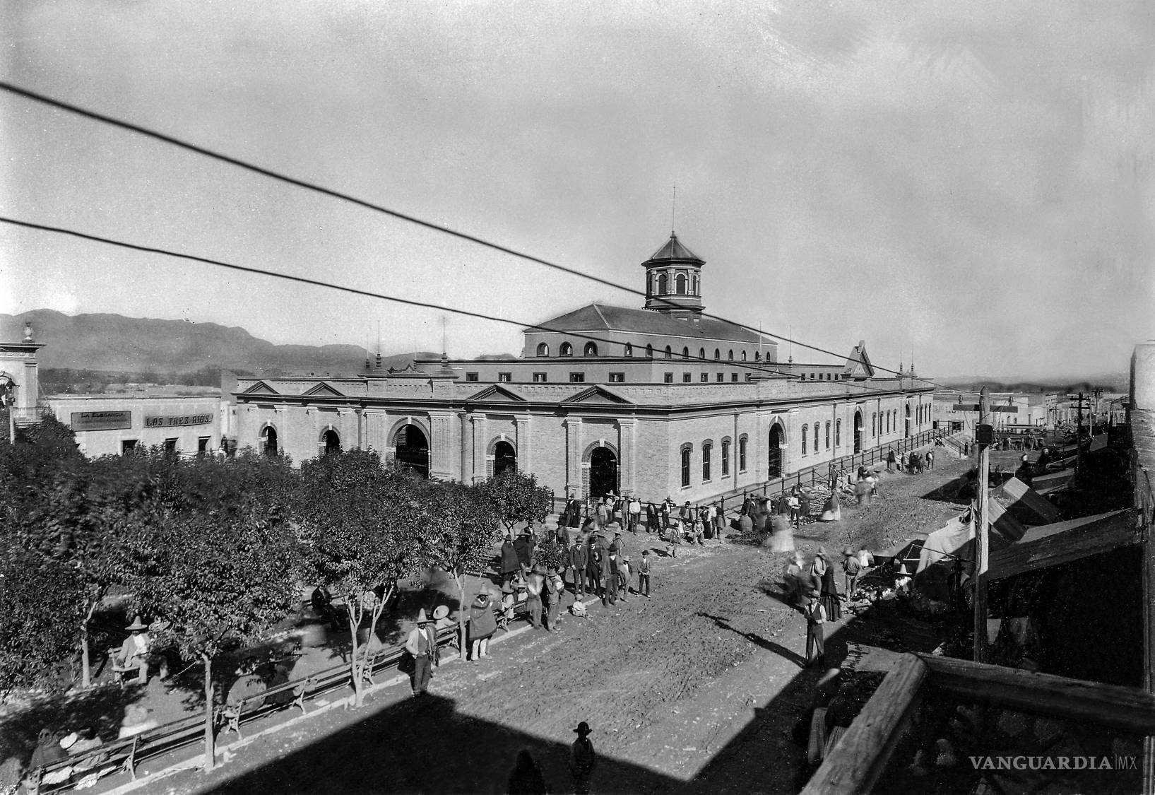 $!La antigua fachada del Mercado Juárez, fotografiada entre 1910 y 1920, muestra un Saltillo donde los tendidos aéreos ya atravesaban las calles y convivían con la arquitectura, los árboles y la actividad comercial. La imagen conserva una etapa temprana de esa transformación del paisaje urbano, cuando los cables comenzaban a formar parte de la vida cotidiana.