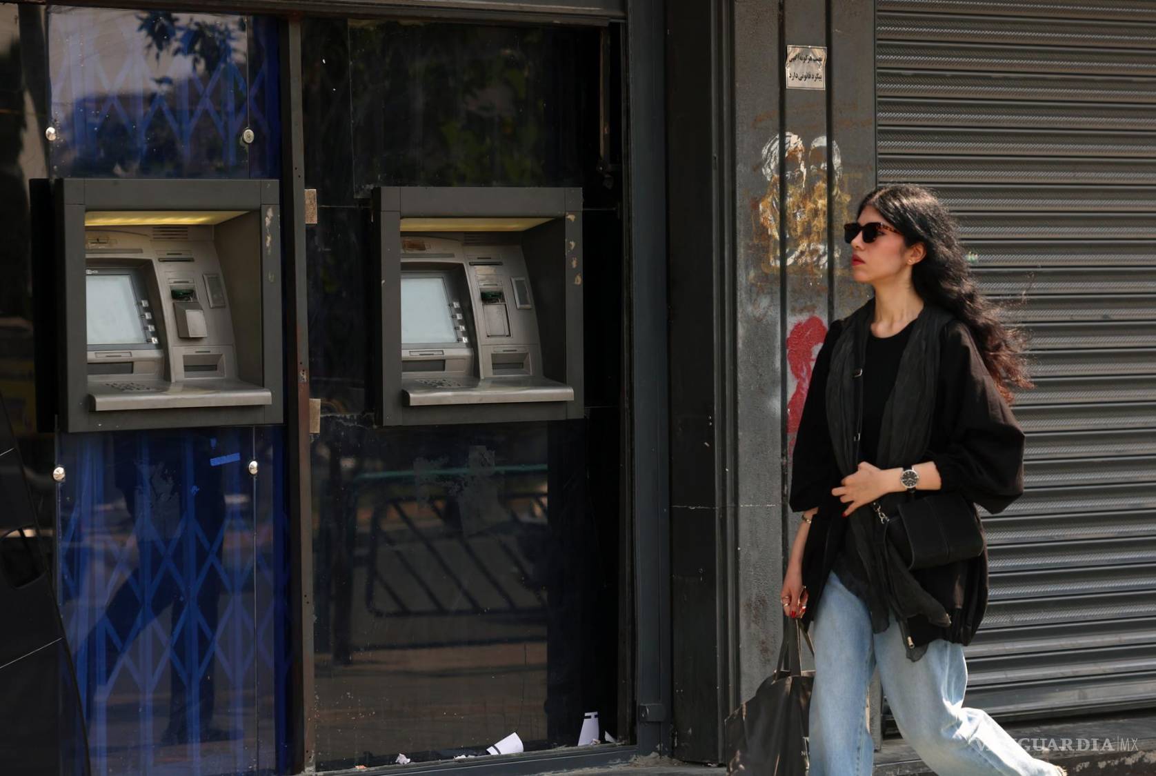$!Una mujer iraní camina junto a un cajero automático en una calle del centro de Teherán, Irán, el 13 de agosto de 2026.