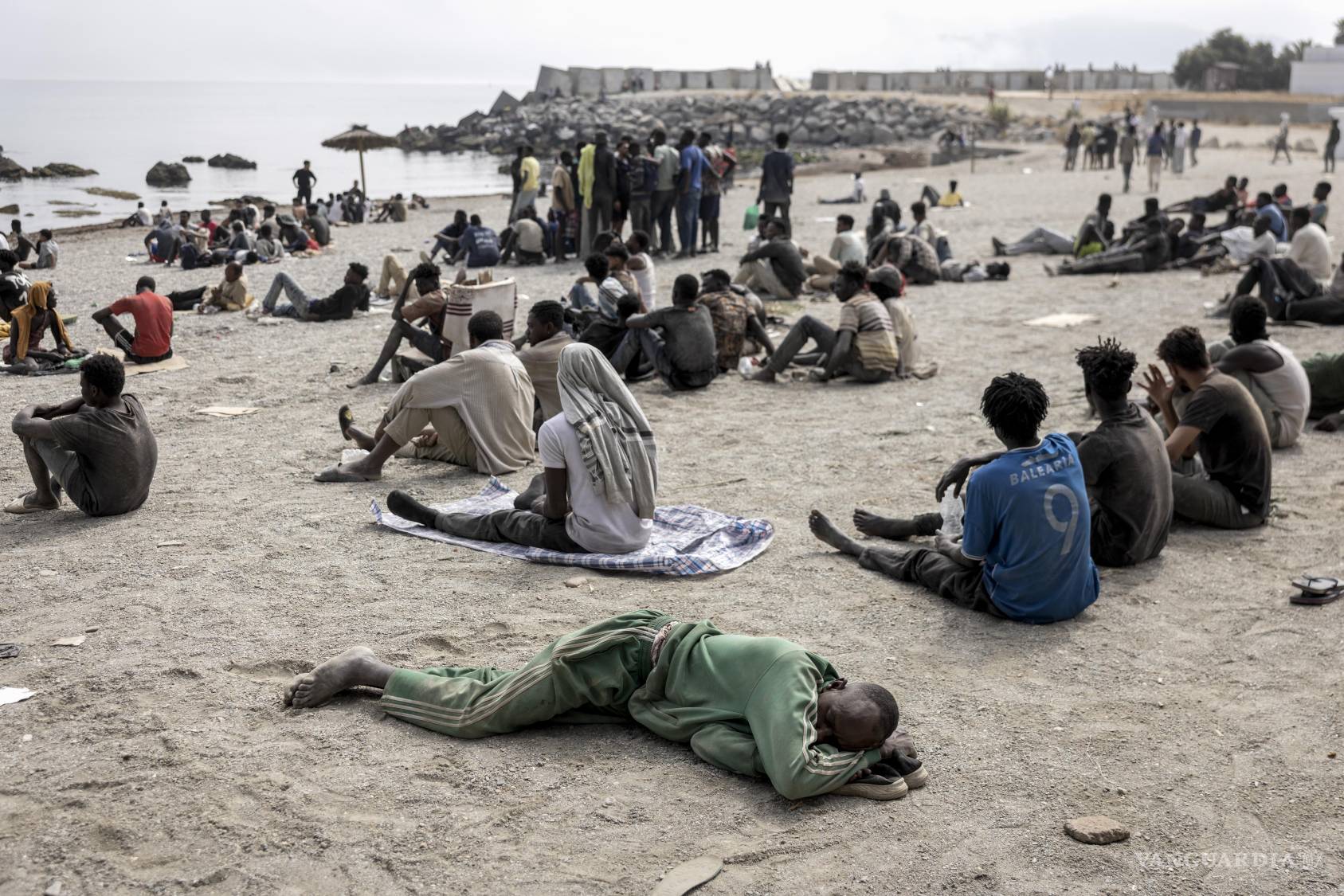 $!Unos migrantes esperan asistencia humanitaria en una playa de Ceuta, territorio español en el norte de África, tras cruzar la frontera desde Marruecos, el 1 de agosto de 2026.