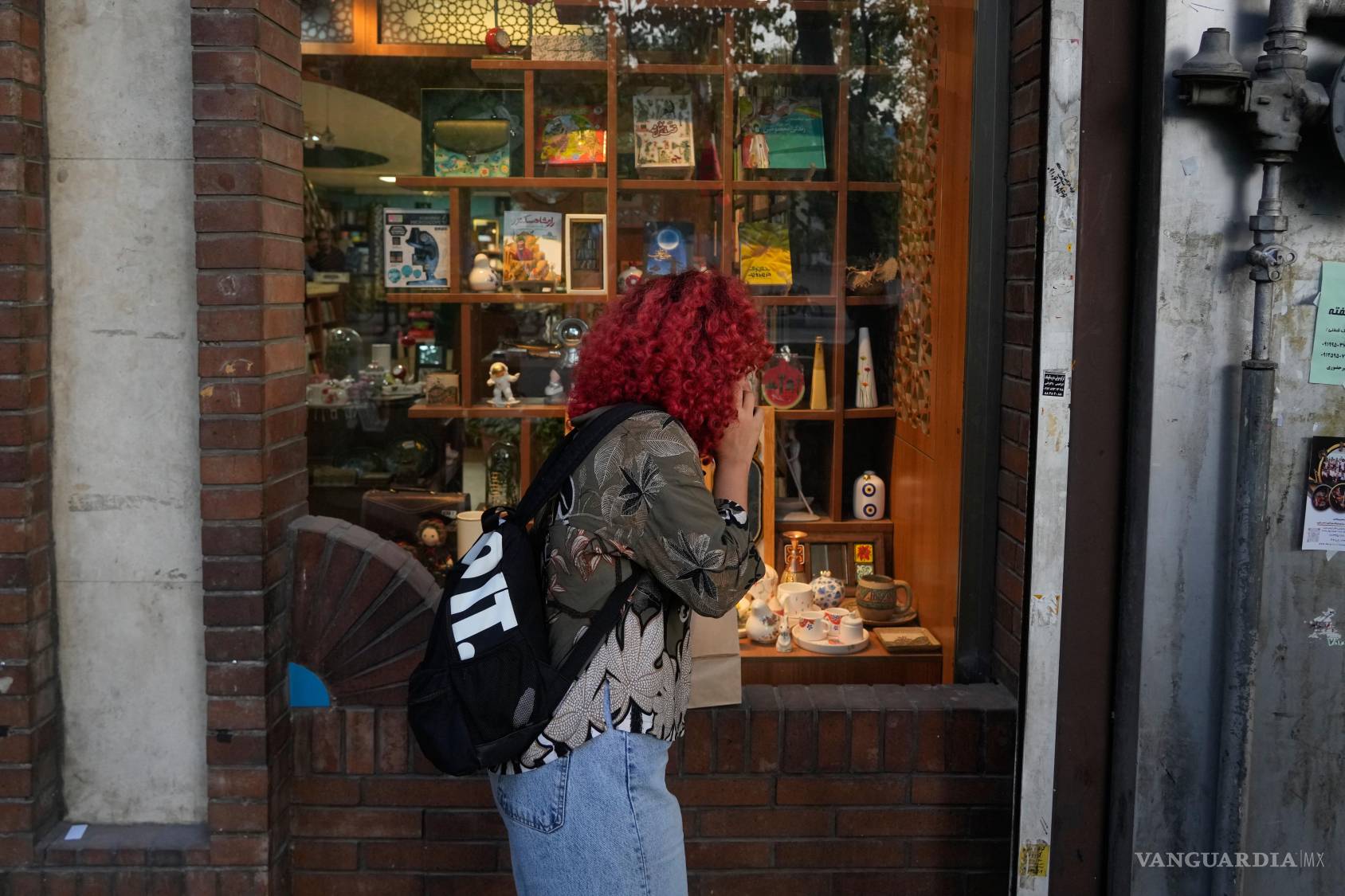 $!Una mujer habla por su teléfono celular mientras mira el escaparate de una tienda en el centro de Teherán, Irán, el martes 12 de mayo de 2026.