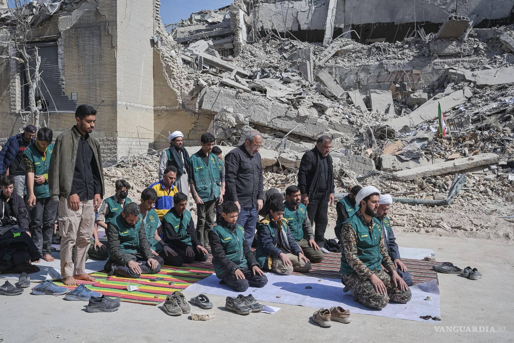 $!Un grupo de voluntarios basijis, milicia islámica, reza al lado de un edificio destruido en los bombardeos israelíes-estadounidenses contra Irán en Teherán.