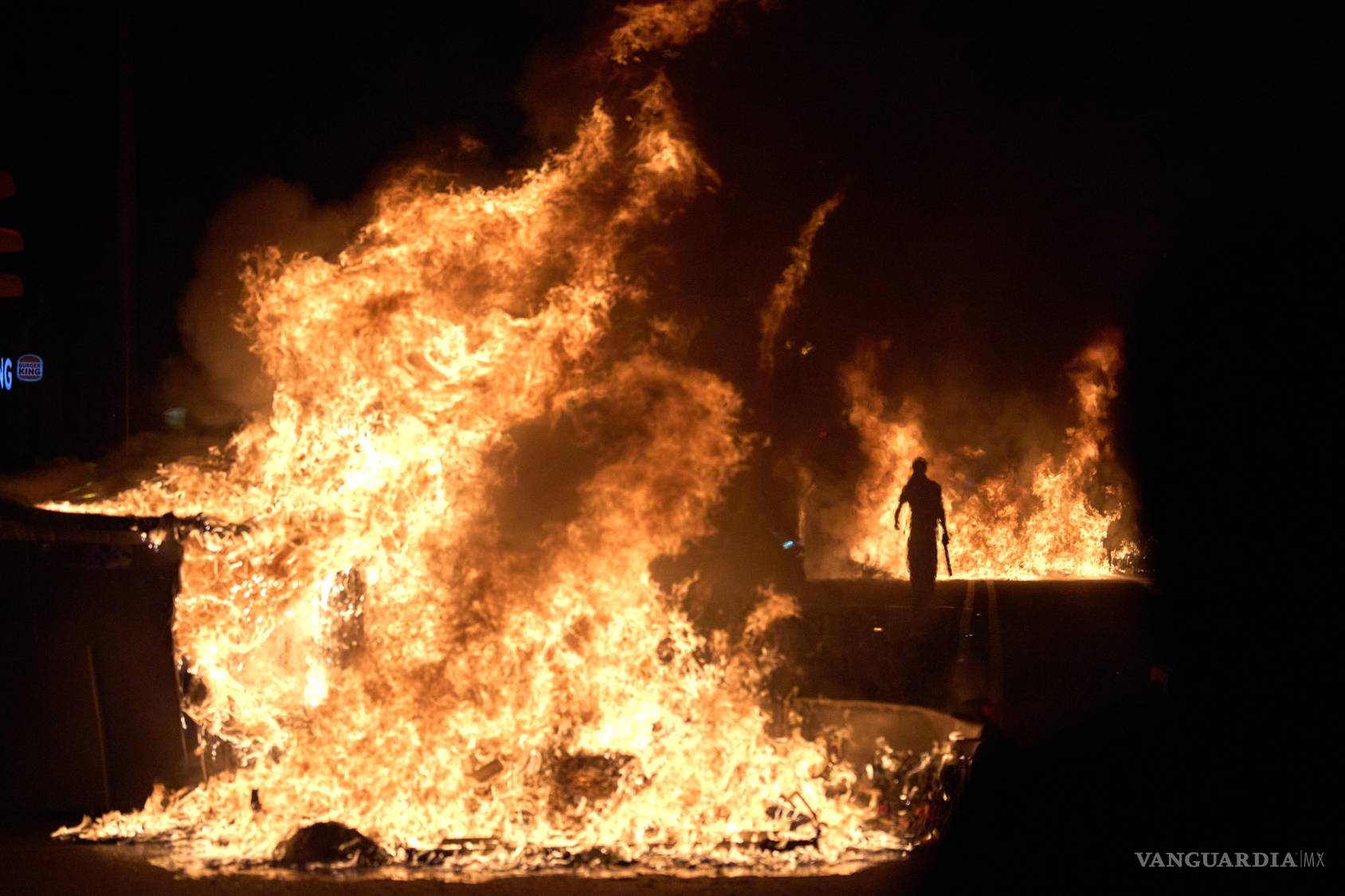$!Una persona pasa junto a contenedores de basura incendiados por manifestantes en protesta de la crisis de vivienda en España.