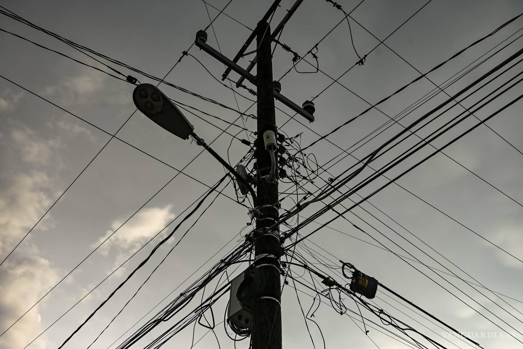 $!En un mismo poste conviven una luminaria moderna, viejos soportes, conexiones recientes y cables de distintas generaciones. La acumulación produce una estética contradictoria: geometrías que alguna vez representaron el futuro y que hoy parecen vestigios de una modernización interminable. Lo nuevo no siempre sustituye a lo viejo. A veces, simplemente se instala encima.