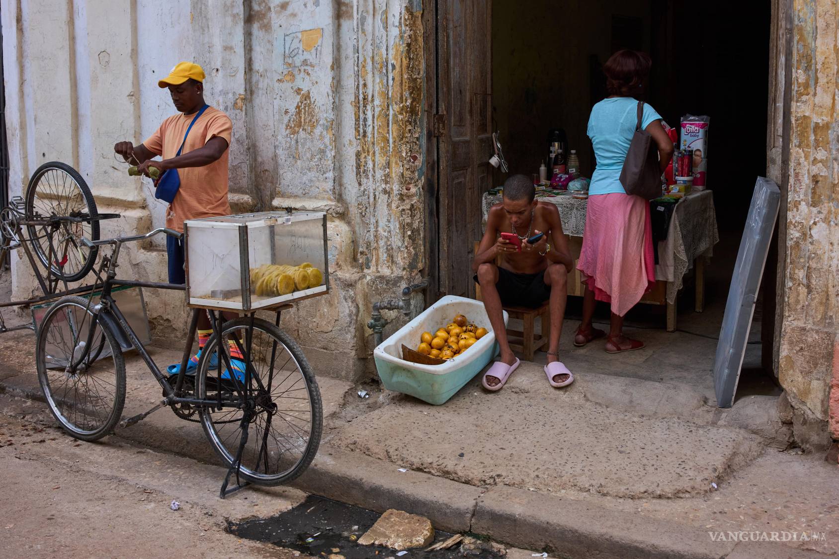 $!Un hombre que vende mangos en la puerta de su casa mira su teléfono mientras espera clientes en La Habana, Cuba.