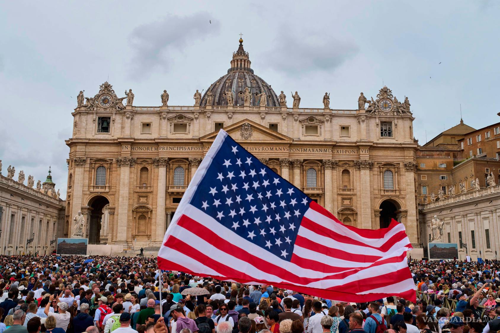 $!Una bandera de EU ondea mientras el papa León XIV aparece en el balcón central de la basílica de San Pedro para su primera bendición dominical tras su elección.