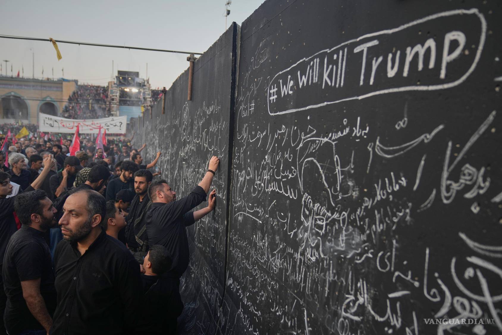 $!En las ceremonias fúnebres del ayatolá Alí Jamenei los asistentes escriben mensajes en una pared, incluyendo uno en inglés que advierte: Mataremos a Trump.