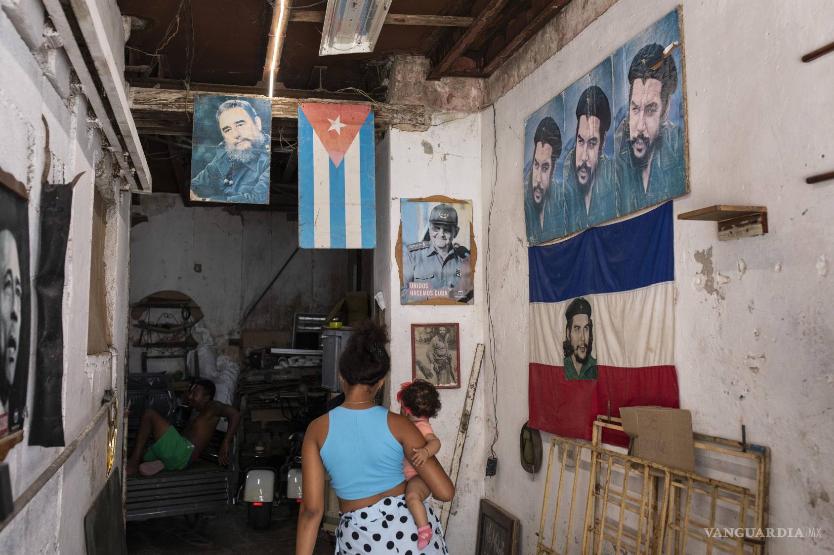 $!Una mujer entra en un taller de muebles con imágenes de Fidel Castro, la bandera cubana, Raúl Castro y Che Guevara, a la derecha, en La Habana.