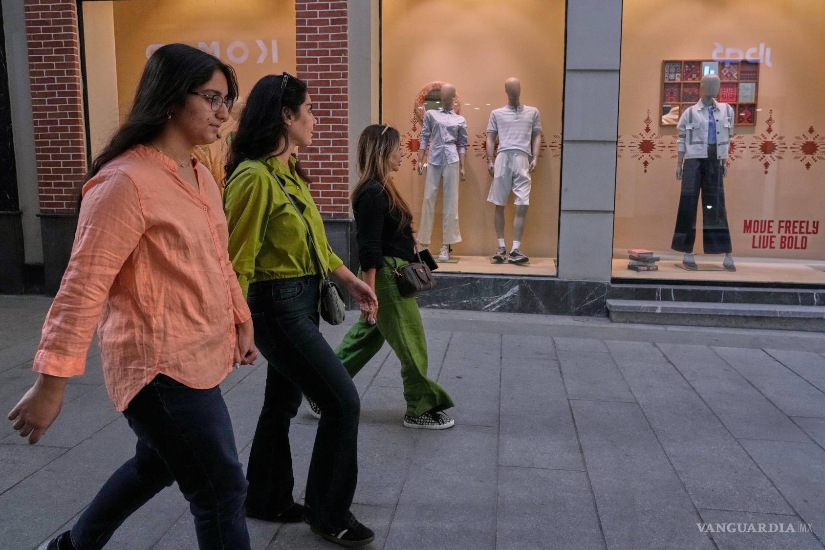 $!Tres mujeres pasan frente a los escaparates de una tienda de ropa en un mercado, el jueves 20 de agosto de 2026, en el norte de Teherán, Irán.