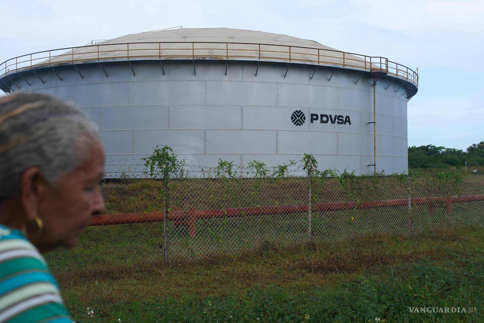 $!Una mujer pasa junto a un tanque de almacenaje de la petrolera estatal venezolana, PDVSA, en Cabimas, Venezuela, el 1 de septiembre de 2026.
