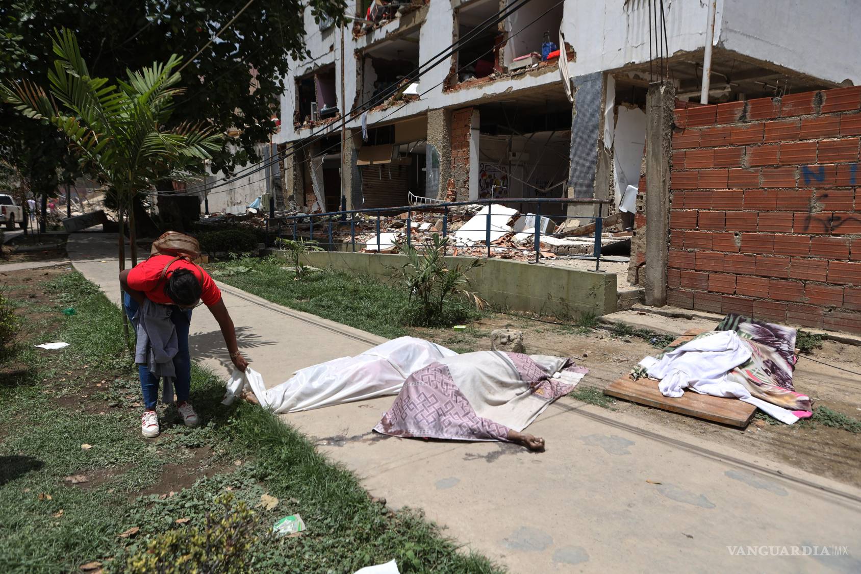 $!Un hombre observa cuerpos cubiertos frente a un edificio dañado al día siguiente de que terremotos y varias réplicas sacudieran La Guaira, Venezuela.