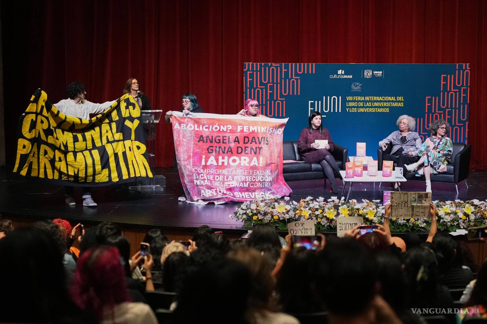 $!Manifestantes exhiben pancartas durante una conferencia de la activista política estadounidense Angela Davis —segunda por la derecha— en la Universidad Nacional Autónoma de México, en la Ciudad de México, el miércoles 26 de agosto de 2026.