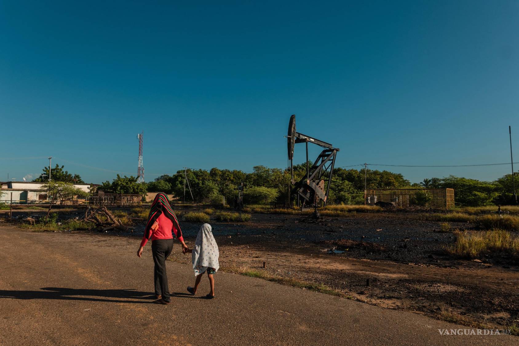 $!Civiles caminan cerca de una infraestructura petrolera dañada en Venezuela; las incursiones aéreas estadounidenses han impactado zonas estratégicas del país.
