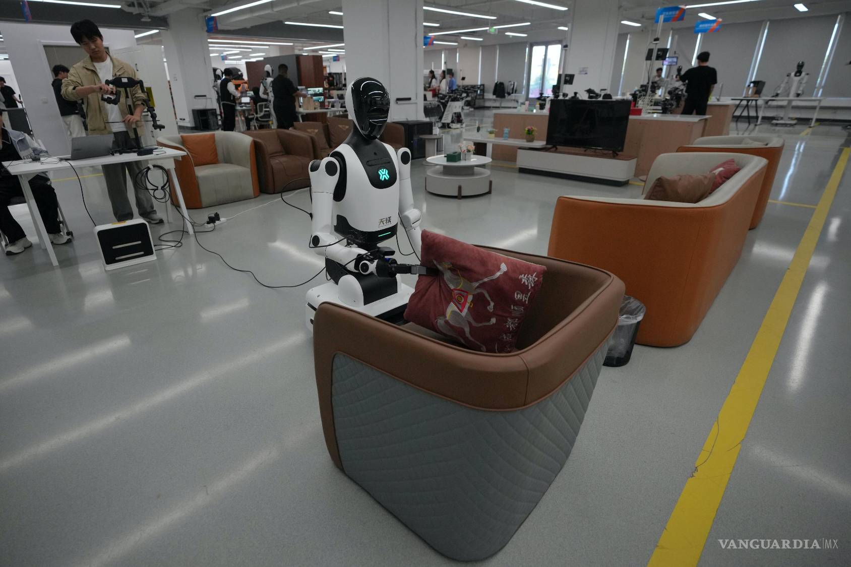 $!Un instructor controla a un robot que ordena una almohada en un sofá en la Base de Datos y Entrenamiento de Robots con Inteligencia Artificial Integrada.