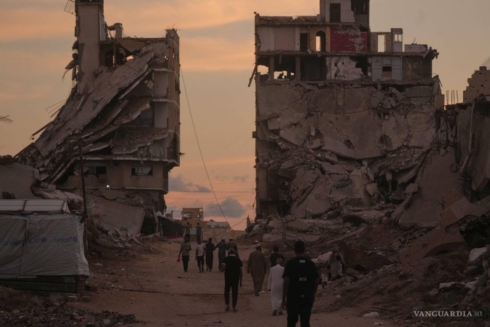 $!Palestinos caminan por una calle rodeada de edificios destruidos en ataques militares israelíes en la ciudad de Gaza, el martes 6 de octubre de 2026.