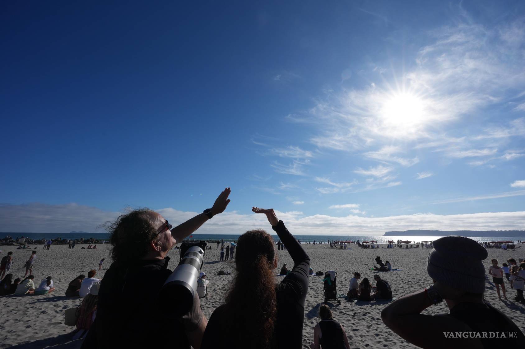 $!Varias personas miran al cielo durante una reunión para ver el regreso de la misión Artemis II de la NASA en Coronado, California.