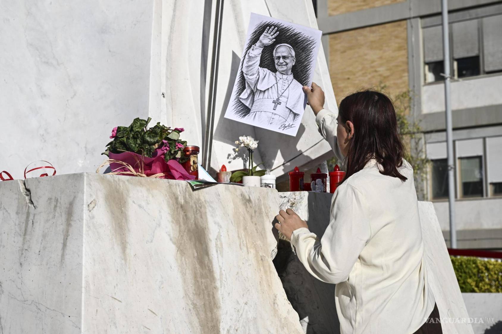 $!Una mujer coloca un retrato del papa León XIX al pie de la estatua del papa Juan Pablo II, en el exterior del Hospital Universitario Agostino Gemelli en Roma.